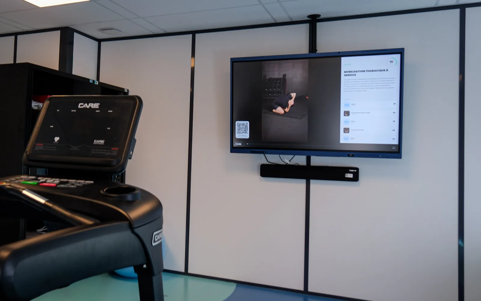 In a client's gym, the wall TV shows the session in progress, with a treadmill in the foreground.